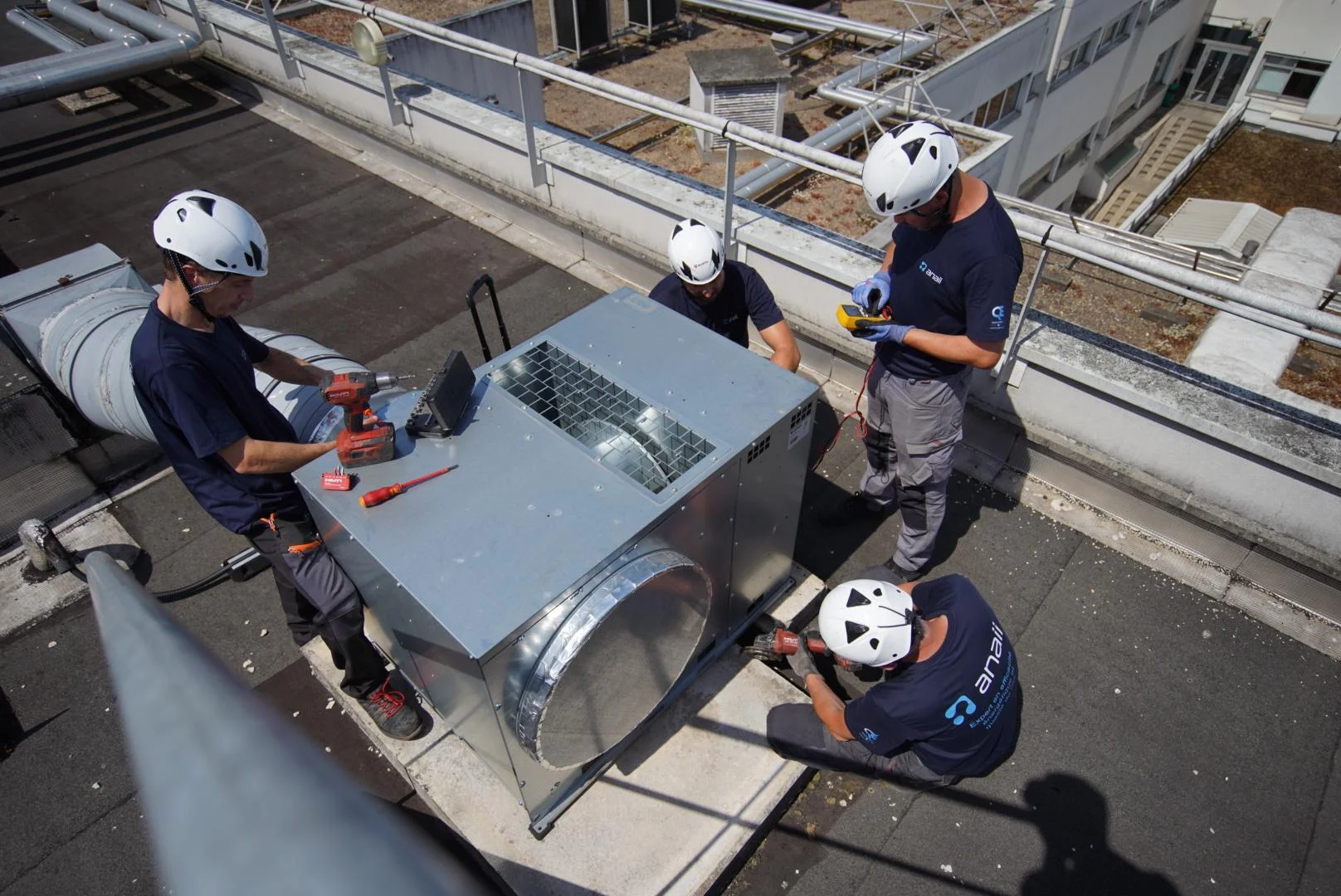 Quatre techniciens ANAII travaillent ensemble autour d’un caisson de ventilation en toiture
